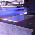 A US25 hot stamp machine is set-up and fixtured to apply Polyfuze onto 6” X 6” HDPE plaques. The Polyfuze graphics are visible on a roll of clear film.